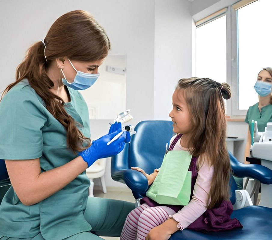 Female dentist showing dental model to young girl during pediatric dental visit