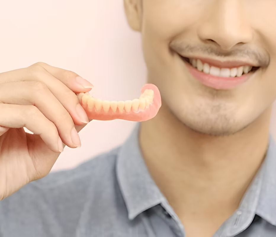 Man smiling while holding a lower full denture