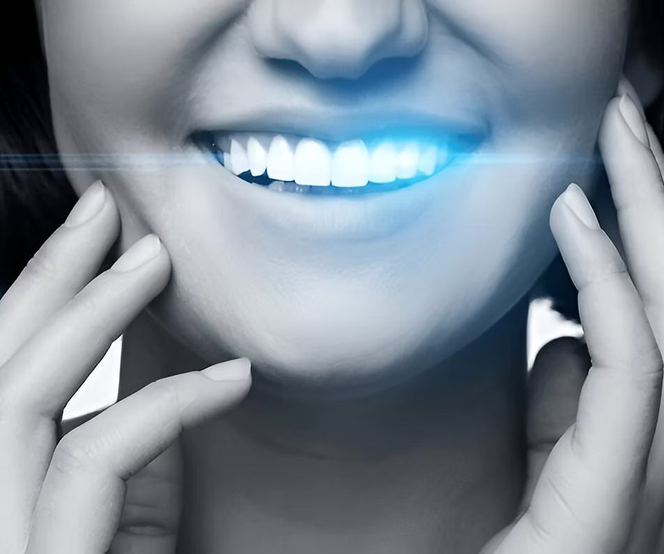 Close-up of a smiling person undergoing teeth whitening with a blue LED light