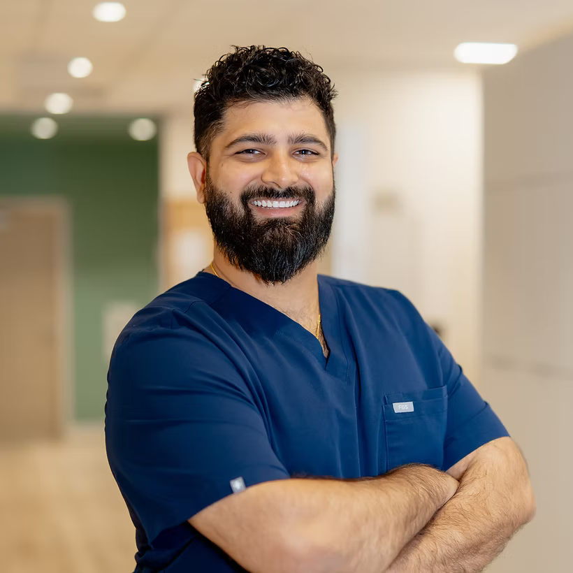 Male dentist in navy blue scrubs with beard and folded arms